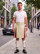A man standing on a city sidewalk wearing a white t-shirt and a beige kilt with red side panels, paired with white knee-high socks and black shoes.