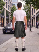 A man viewed from behind wearing a white t-shirt, a dark green pleated leather kilt, white knee-high socks, and black shoes, standing on a city sidewalk.