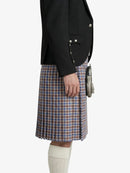 Person wearing a black blazer and plaid kilt on a white background