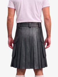 A person shown from the back wearing a dark gray pleated leather kilt with side cargo pockets, paired with a light pink t-shirt and white socks, against a plain light gray background.