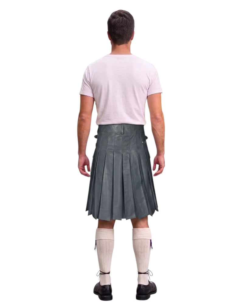 A man shown from the back wearing a gray pleated kilt, a light pink t-shirt, white knee-high socks, and black shoes, against a plain white background.