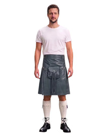 A man modeling a dark gray faux-leather kilt with a front pouch pocket, paired with a white t-shirt, cream knee-high socks, and black lace-up shoes, against a solid white background.