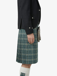 Person wearing a black jacket and green plaid kilt on a white background