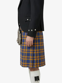 Person wearing a black jacket and blue and orange plaid kilt on a white background