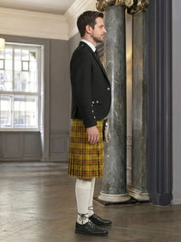 Man wearing a black jacket and yellow plaid kilt in an elegant interior setting.
