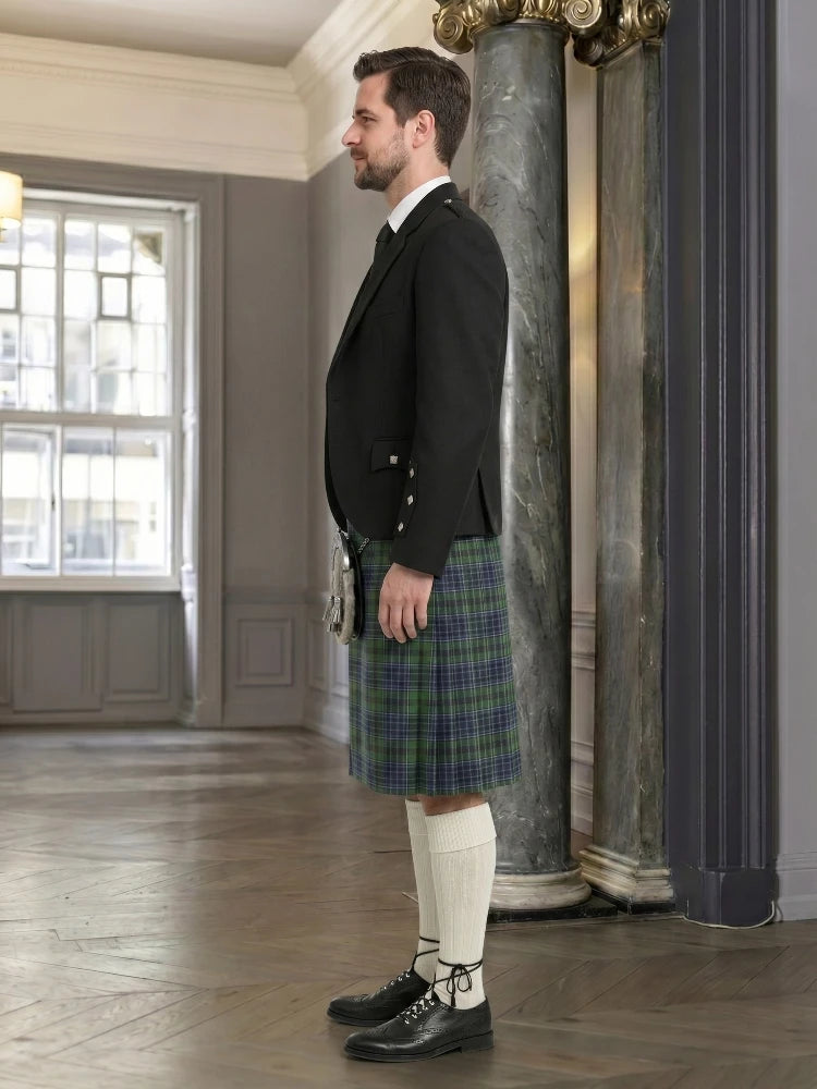 Man wearing a black jacket, plaid kilt, and white knee-high socks in an elegant room.