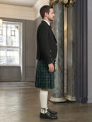 Man wearing a black jacket, green plaid kilt, and white knee-high socks in an elegant room.
