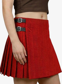 Red pleated skirt with black buckles worn by a person on a white background