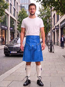 A man standing on a city sidewalk wearing a bright blue leather kilt with a white t-shirt, white knee-high socks, and black leather shoes. The background shows a street scene with buildings, a parked black Mercedes, and a bicycle.