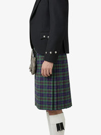 Person wearing a dark jacket and green plaid kilt on a white background