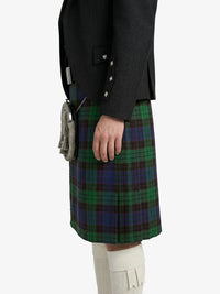 Person wearing a dark coat and green plaid kilt on a white background