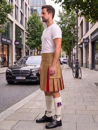 A man wearing a tan pleated kilt with red side panels, a white t-shirt, white knee-high socks, and black shoes, standing on a city sidewalk next to a street with a Mercedes-Benz and trees.